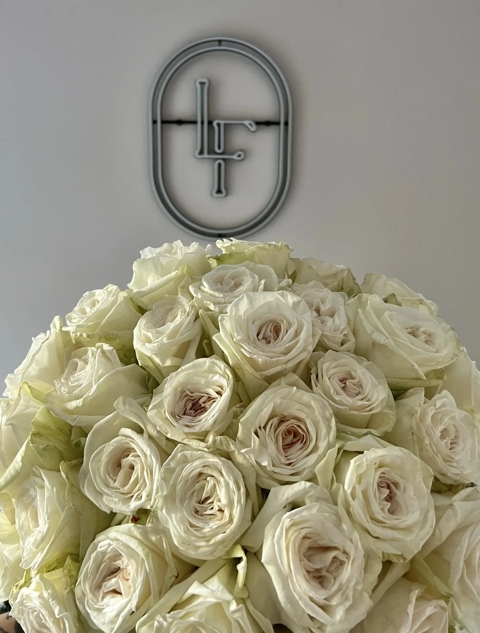 Close-up of full White O’Hara roses with creamy white petals and soft blush centers, placed below the Lu La Fleur neon logo